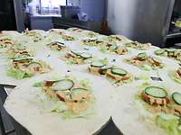Die vorbereiteten Wraps warten auf das Fleisch Viele Wraps liegen auf einem Tisch. Es ist schon Salat, Gurke, Tomate und Soße drauf. Das Fleisch fehlt noch.